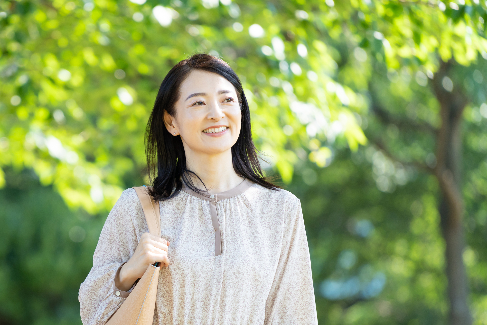新緑の中を気持ちよさそうに笑顔で歩く女性
