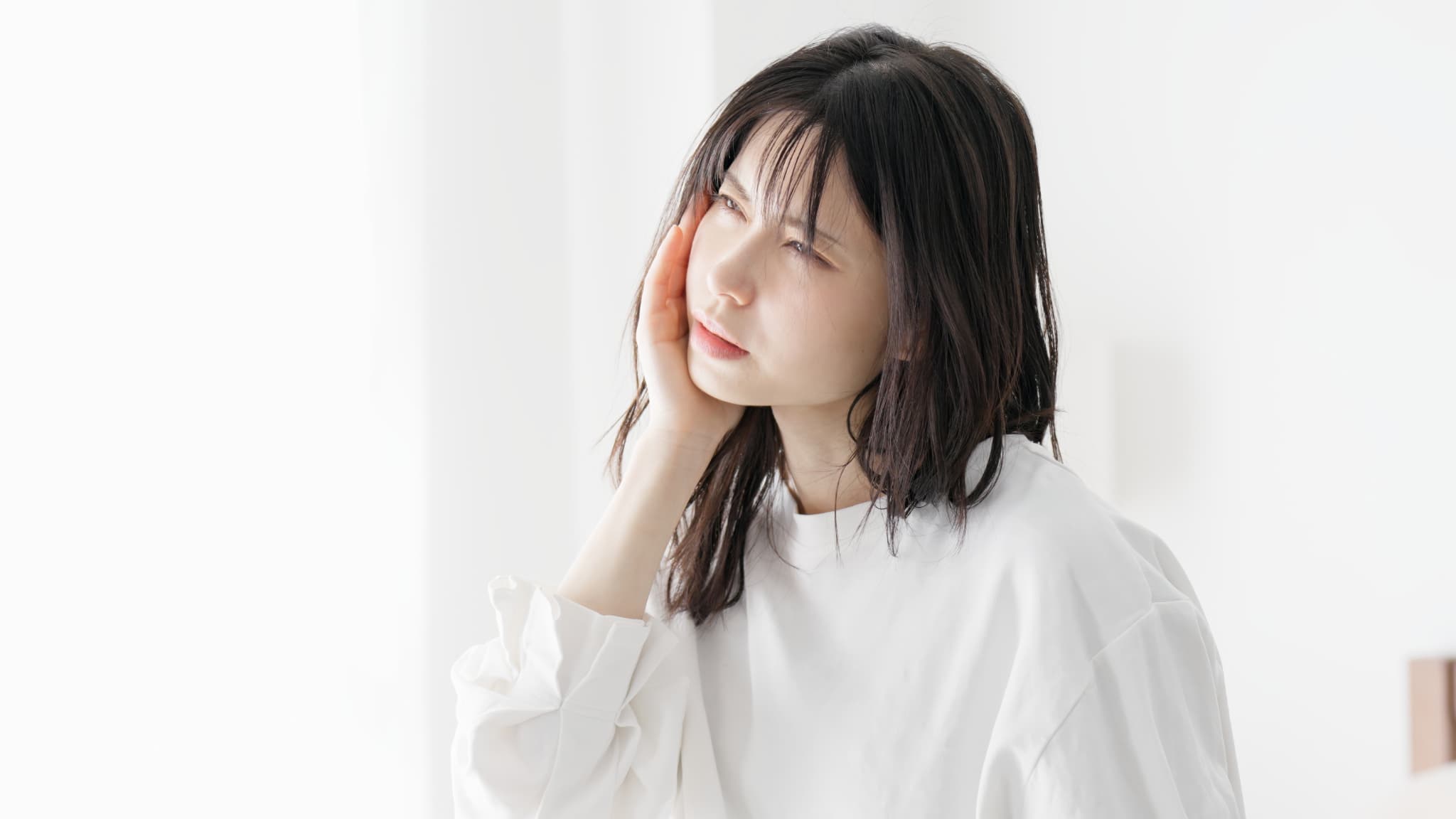顎関節を押さえて不快そうな顔の女性