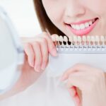 シェードガイドを当てて鏡で歯の色をチェックする女性