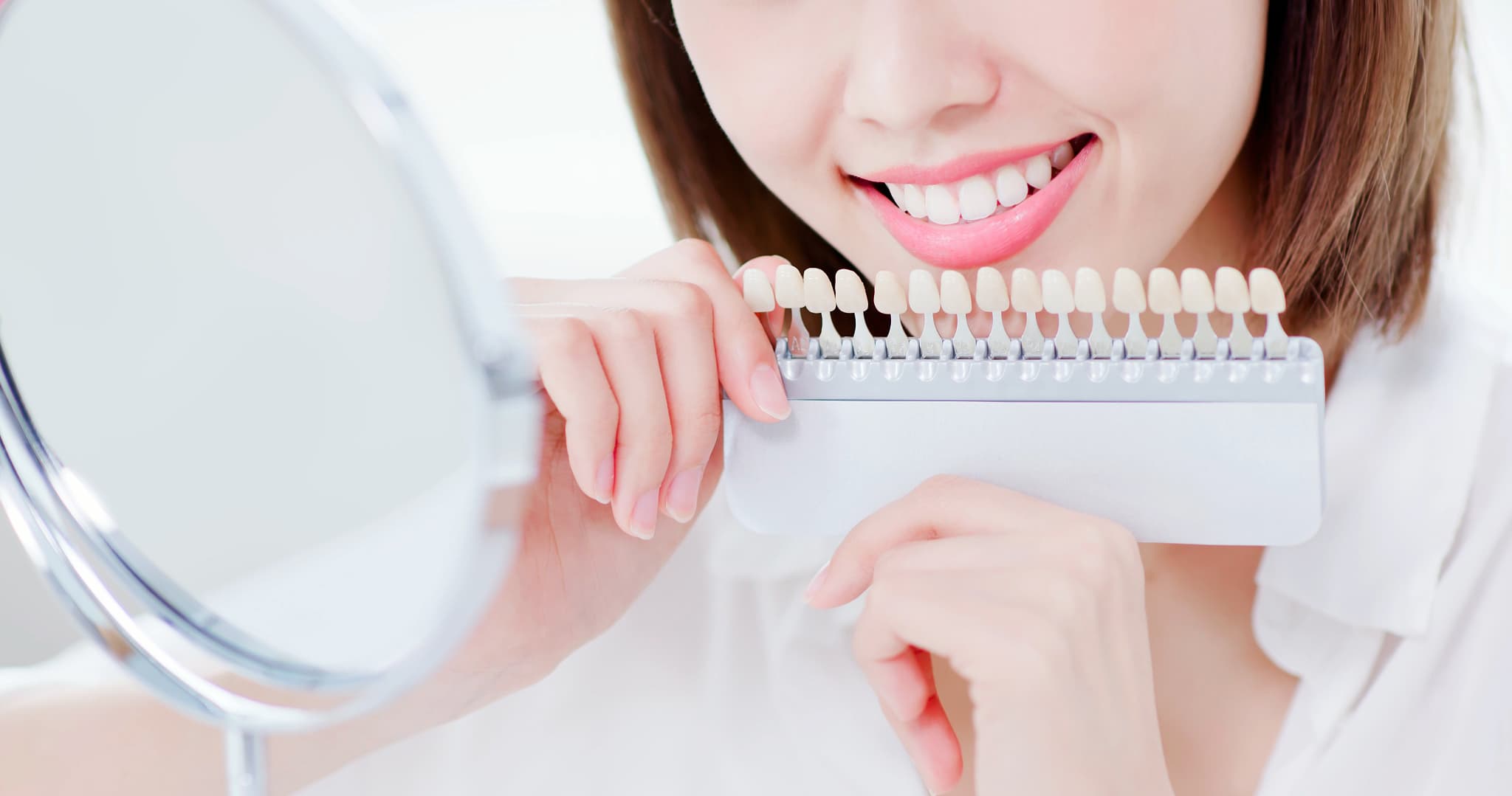 シェードガイドを当てて鏡で歯の色をチェックする女性